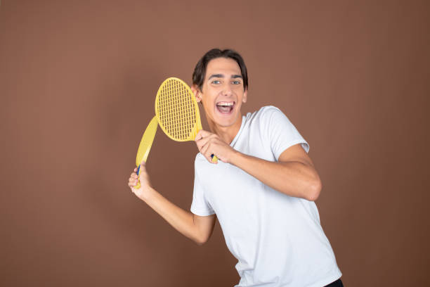 istock Funny guy with children's tennis rackets posing on a brown background. 1854735335