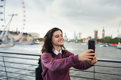 Happy young tourist taking a selfie in front of the London Eye wheel.