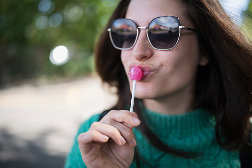 Close up of a dark-haired pretty lady licking a swirl lollipop with her eyes closed during the studio photo shoot. Sweet food concept