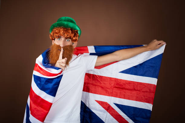 istock St.Patrick 's Day. Funny guy in a leprechaun costume posing on a brown background. 1854740599