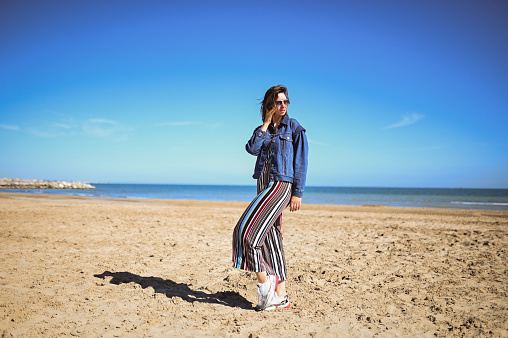 young woman in a jeans jacket standing on the beach.