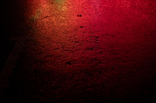 Red light on wet asphalt. Asphalt in a red glow in the evening. Empty parking space. Road surface texture.