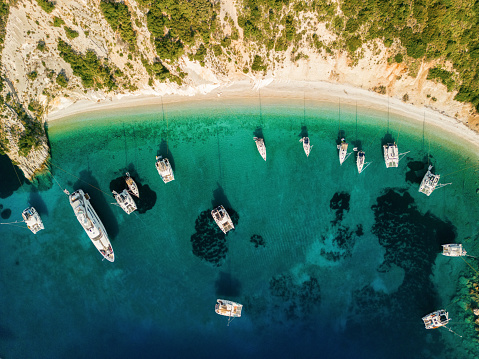 Sailboats anchored in a beautiful Filiatro bay, Greece. It's a beautiful sunny day, the sea is blue and turquoise green, and crystal clear.