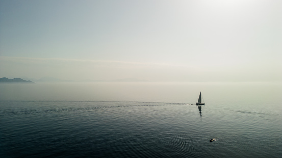 A sailboat anchored in a bay on a misty day, near Ithaca, in the Ionian sea. There is a special, mystery atmosphere around it.