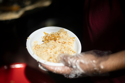 Rice in a plate. Cook on the street. Hand in glove for food. Food distribution in the city.