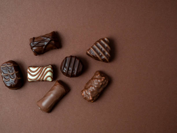 A varied assortment of chocolates arranged on a rich brown background.