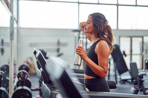 latin woman walking on a treadmill drinking water and holding her hair