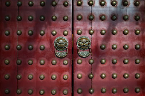 Red antique Chinese doors with brass lion head door knockers and gilded studs.