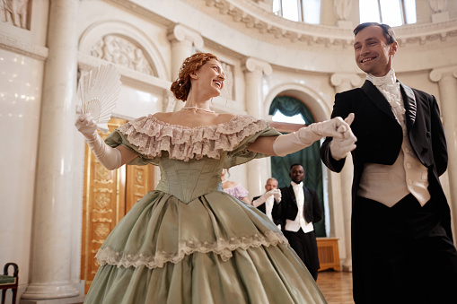 Low angle portrait of beautiful renaissance couple dancing together enjoying ball in palace