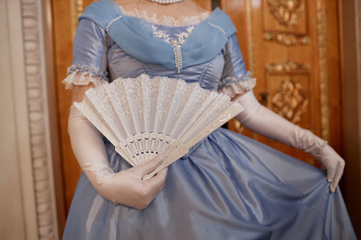 Close up of lady wearing blue ballgown curtsying and holding fal in palace, copy space