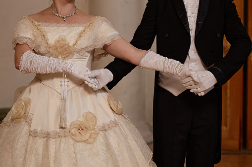 Closeup of classic young lady and gentleman holding hands dancing together in ballroom