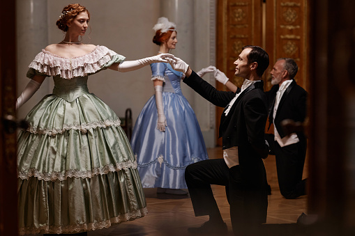 Side view portrait of ladies and gentlemen dancing in palace ball with ambient lighting