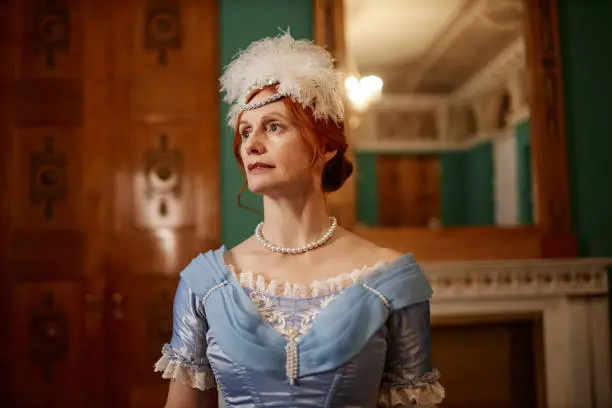 Waist up portrait of red haired senior lady wearing ballgown and looking away, copy space