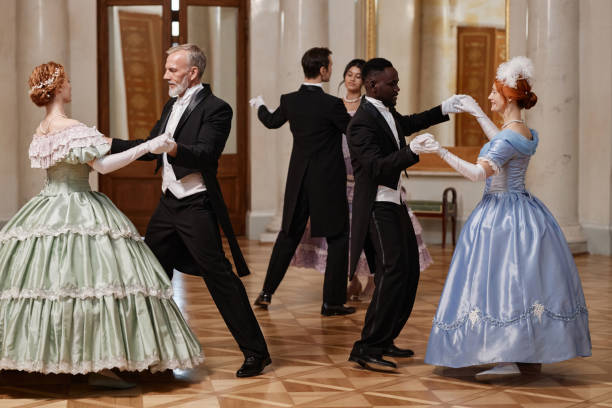 A female dancer in a black dress gracefully raises her arms in an elegant pose inside a spacious dance hall. With a focused expression and poised stance, she embodies the art of movement and expression.