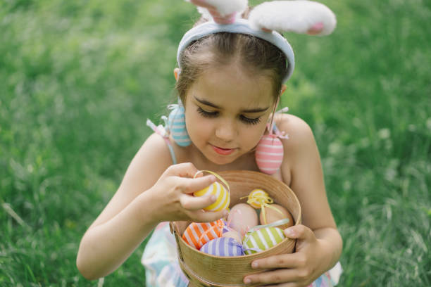 istock Funny girl with eggs basket and bunny ears on Easter egg hunt in garden. 1854881068
