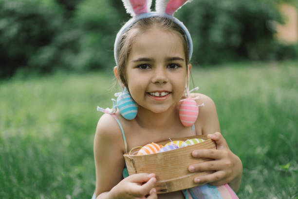 istock Funny girl with eggs basket and bunny ears on Easter egg hunt in garden. 1854881069
