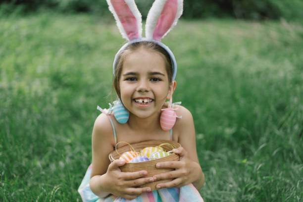 istock Funny girl with eggs basket and bunny ears on Easter egg hunt in garden. 1854881075