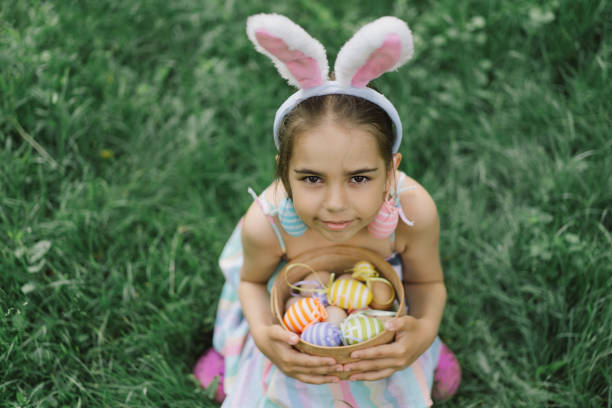 istock Funny girl with eggs basket and bunny ears on Easter egg hunt in garden. 1854881084