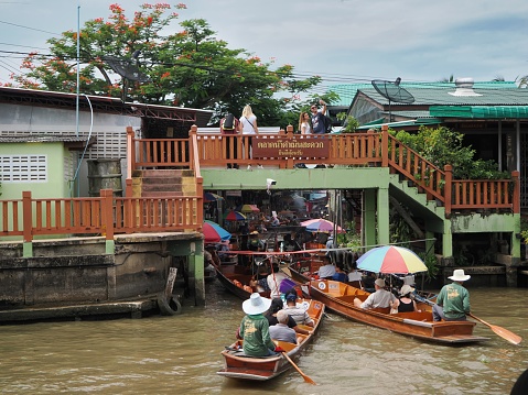 Ratchaburi, Thailand - July 26, 2023: Tourists visit the floating market by boarding the boats and walk on the bridge. The Thai letters on the bridge means welcome to Damnoen Saduak Floating Market.