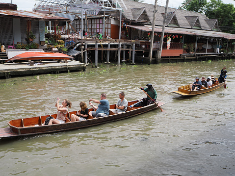 Ratchaburi, Thailand - July 26, 2023: Tourists board the boat for boat tour along the Damnoen Saduak canal close to the busy floating market.