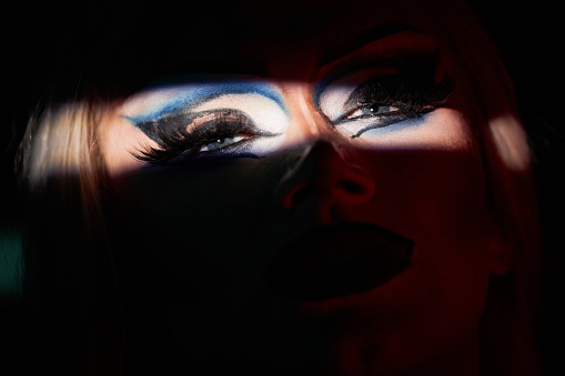 Spotlight detail shot of drag queen performer on stage with focus on eyes with extravagant make up, copy space