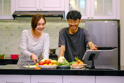 Asian couples cooking together and looking at digital tablet for recipes. Circular habits in the kitchen.