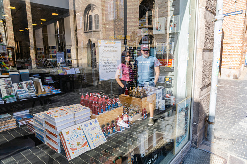 Showcase of a souvenirs shop with books and souvenirs and reflection of people on the window. Copenhagen, Denmark - September 30, 2023