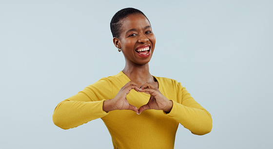 Happy black woman, portrait and heart hands for love, care or romance against a gray studio background. Face of African female person or model showing like emoji, shape or romantic gesture on mockup