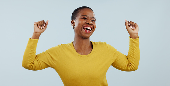 Excited black woman, dancing and celebration for winning or promotion against a gray studio background. Face of happy African female person or model in joy or satisfaction for bonus or good news