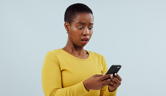 Black woman, phone and shocking news on social media, terrifying or bad against a studio background. Face of surprised African female person or model on mobile smartphone for alert or notification