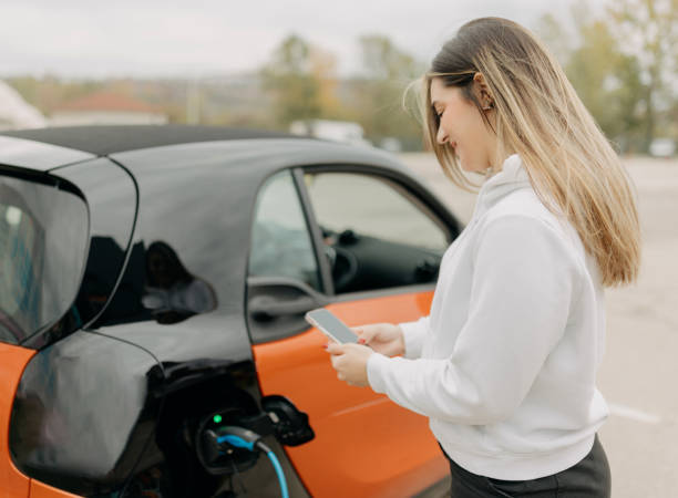 istock Young woman using mobile phone while charging the car 1855021873