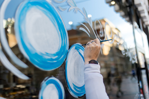 The artist uses paint to decorate the shop window for the winter Christmas season.
