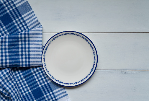 Top view of blank dish and blue tablecloth on a wood background