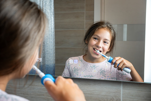 Happy little girl brushing her teeth in front of a bathroom mirror. Morning hygiene.