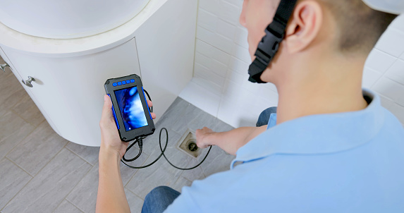 asian male home inspector is using endoscope inspection camera to check bathroom tube