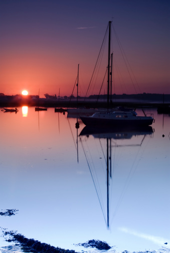 Taken during sunrise, this spring scene shows a row of sailing yachts moored in the river Deben at Walderingfield, Suffolk on a still, clear morning. The picture shows the clam of the early morning waters, orange coloured sky and first rays of sunlight reflected in the river