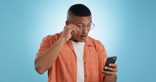 istock Surprise, glasses and man with smartphone, internet and reaction with expression on a blue background. Person, guy and model with a cellphone, email and announcement with post, blog and digital app 1855093981