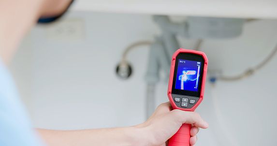 close up asian male home inspector is using thermal imager to check water leakage situation at kitchen sink tube