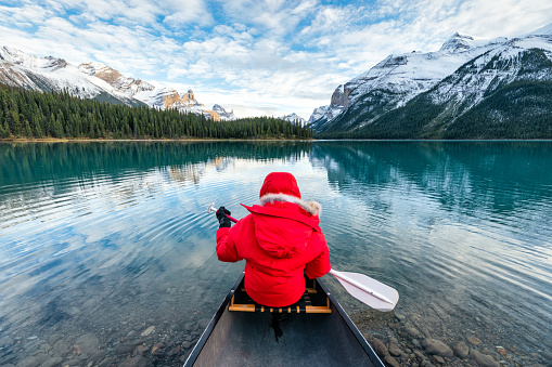 Rear view of male tourist in red winter coat canoeing with paddle in Spirit Island on Maligne Lake at Jasper national park, Alberta, Canada