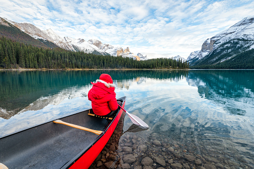 Rear view of male tourist in red winter coat canoeing with paddle in Spirit Island on Maligne Lake at Jasper national park, Alberta, Canada