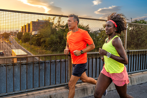 African american woman and asian man jogging together, running across urban bridge at sunset