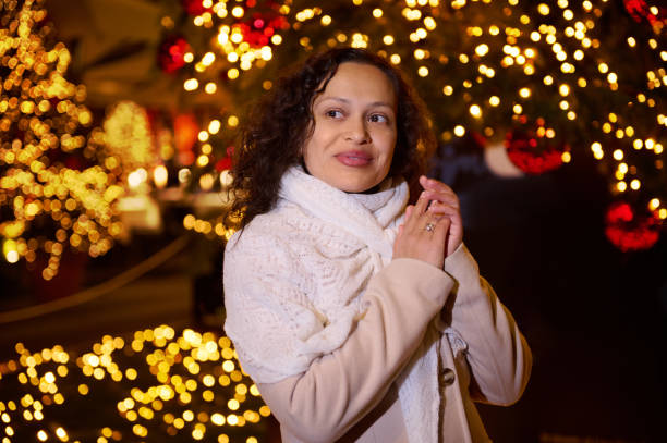 Smiling happy woman walking in Christmas market decorated with holiday lights in the evening. Feeling happy in big city.