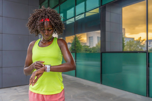African american sportswoman checking smart watch while jogging outdoors, medium shot