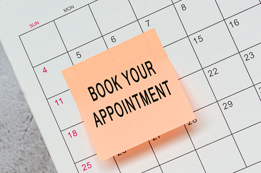 Book your appointment text on orange paper sticky note and stuck to a calendar background. Reminder concept.