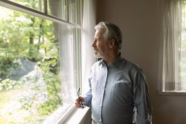 istock Pensive older man stand by window admire sunny day outside 1855129467