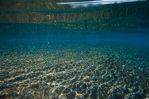 Underwater view crystal sea with stones bottom and reflection on surface.