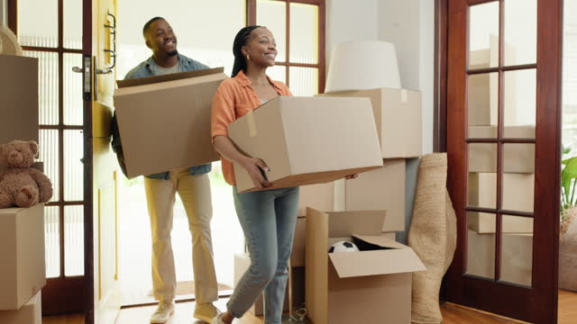 Happy couple, walking or smile with boxes in new house, cardboard or love in living room with care. Black people, man or woman to enter in apartment, relocation or pride for investing in real estate