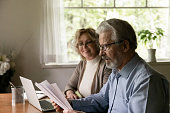 Smiling aged wife watching surprised senior husband reading paper letter