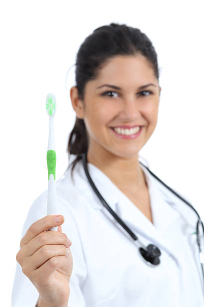 belle femme médecin dentiste en tenant une brosse à dents et montrer - smiling human teeth toothbrush moving up photos et images de collection