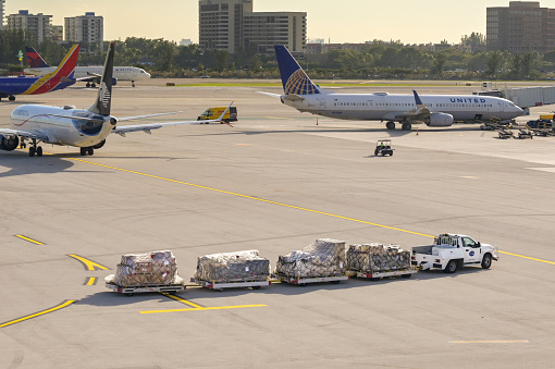 Miami, Florida, USA - 4 December 2023: Truck towing trailers with air cargo pallets at Miami International Airport